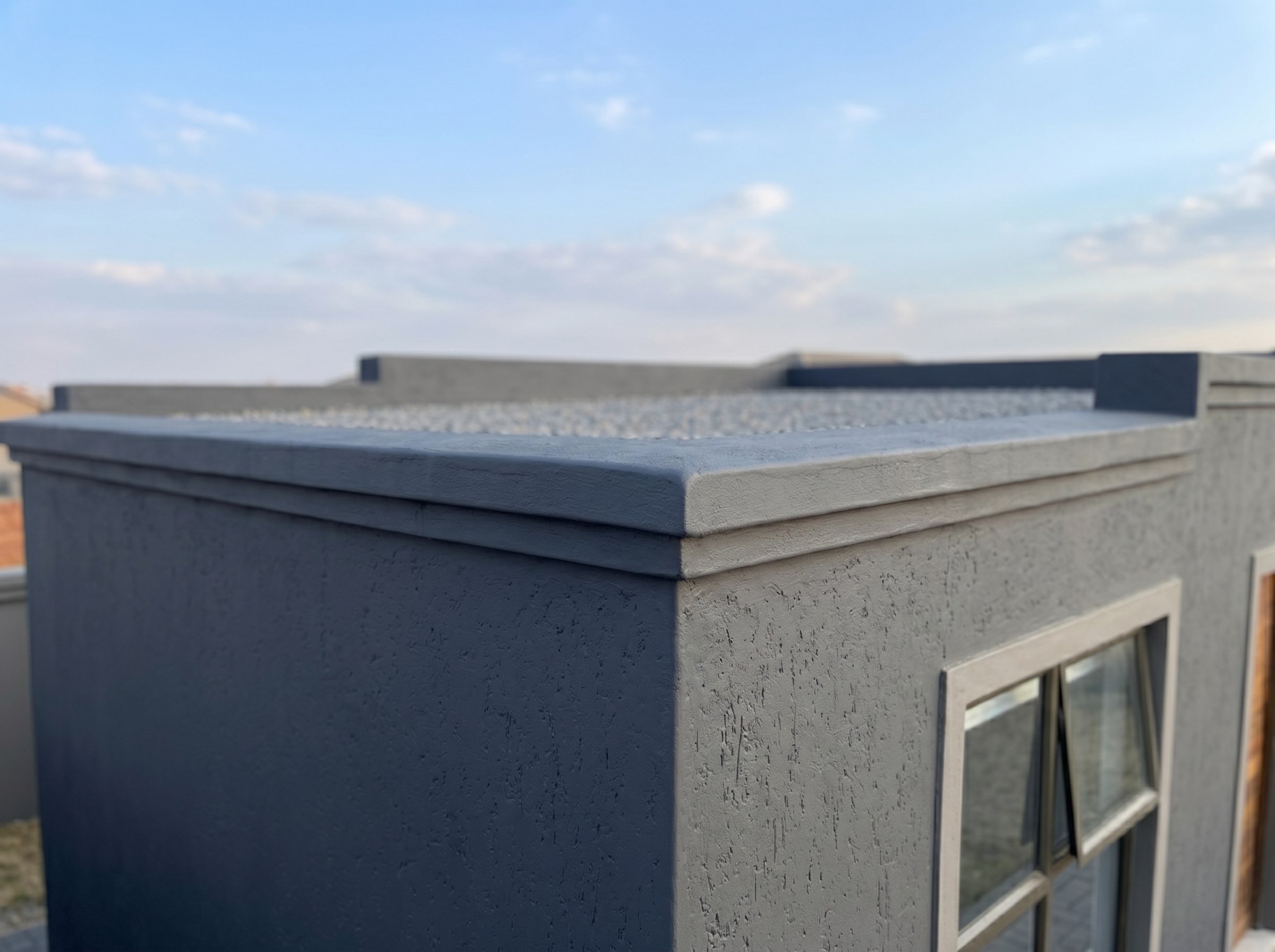 Completed parapet cap and cement finish on a small flat-roof building